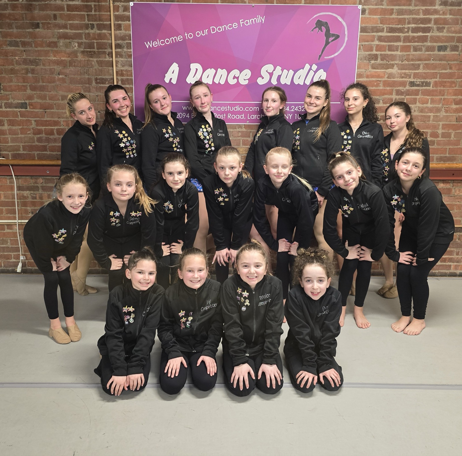 A Dance Studio dancers in team jackets in front of the Welcome to our Dance Family banner